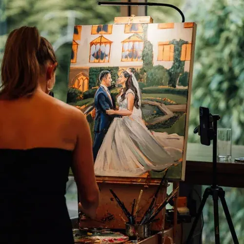 A wedding painter works at an easel beside a painting of a couple.