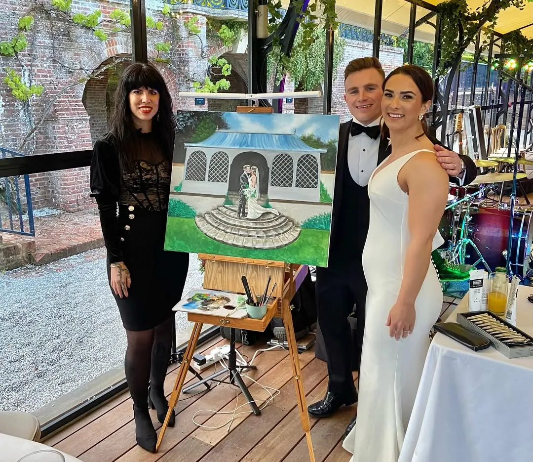 A couple and their artist pose beside the completed painting of their wedding venue.