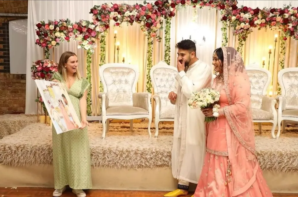 A couple react with delight as their artist reveals their wedding painting beneath a floral arch.